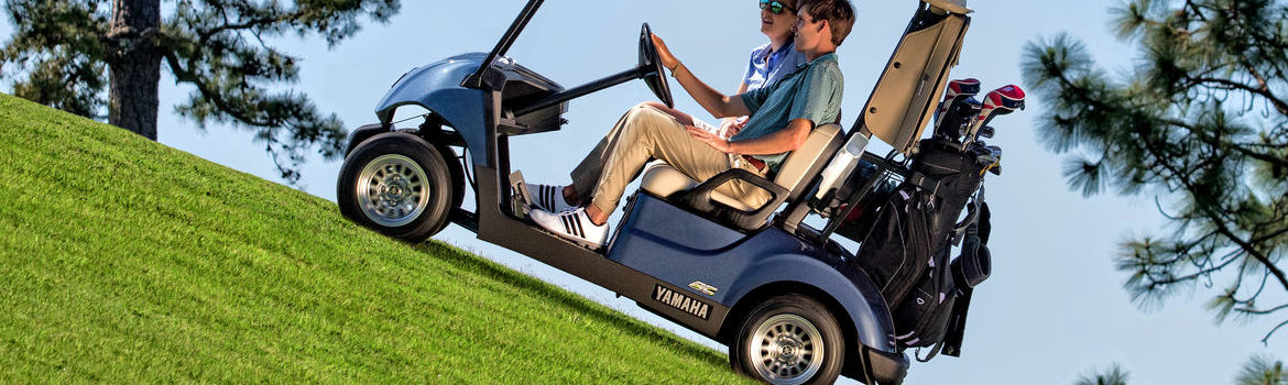 Two people riding up a hill in a 2018 Yamaha Golf Car.